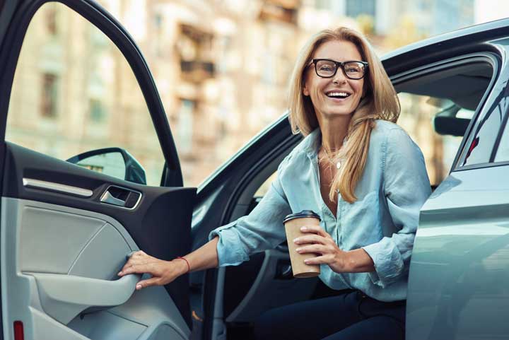 Woman getting out of car with coffee