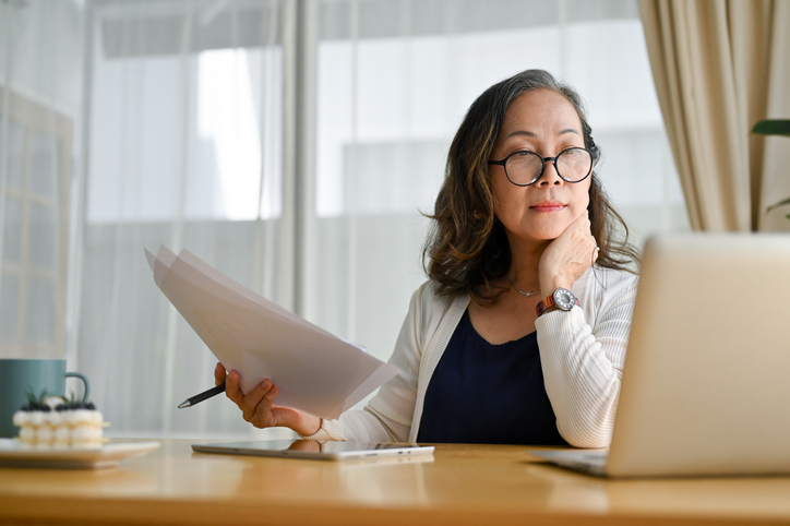 Woman holding paper while looking at computer screen. Changes to the VAT online account are effective 15th May 2023. Talk to Harrow based RA Accountants about VAT and Making Tax Digital.